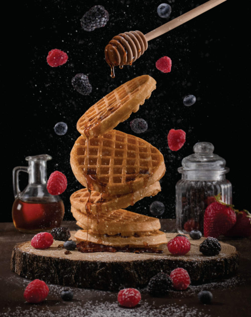 Fotografía tipo bodegón de unos waffles con fruta cayendo.