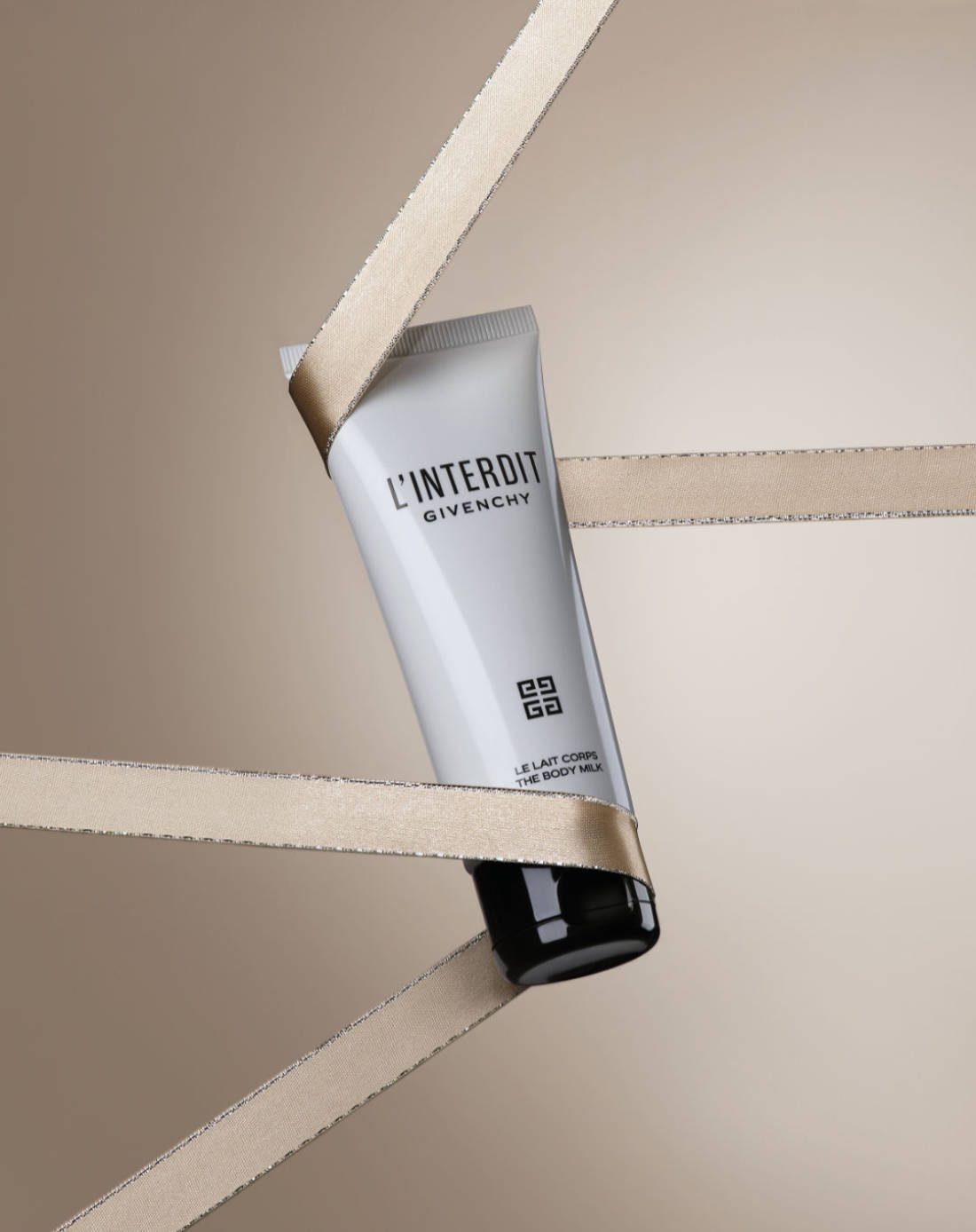 Fotografía primer plano de la crema corporal L'interdit de Givenchy envuelta en listones.