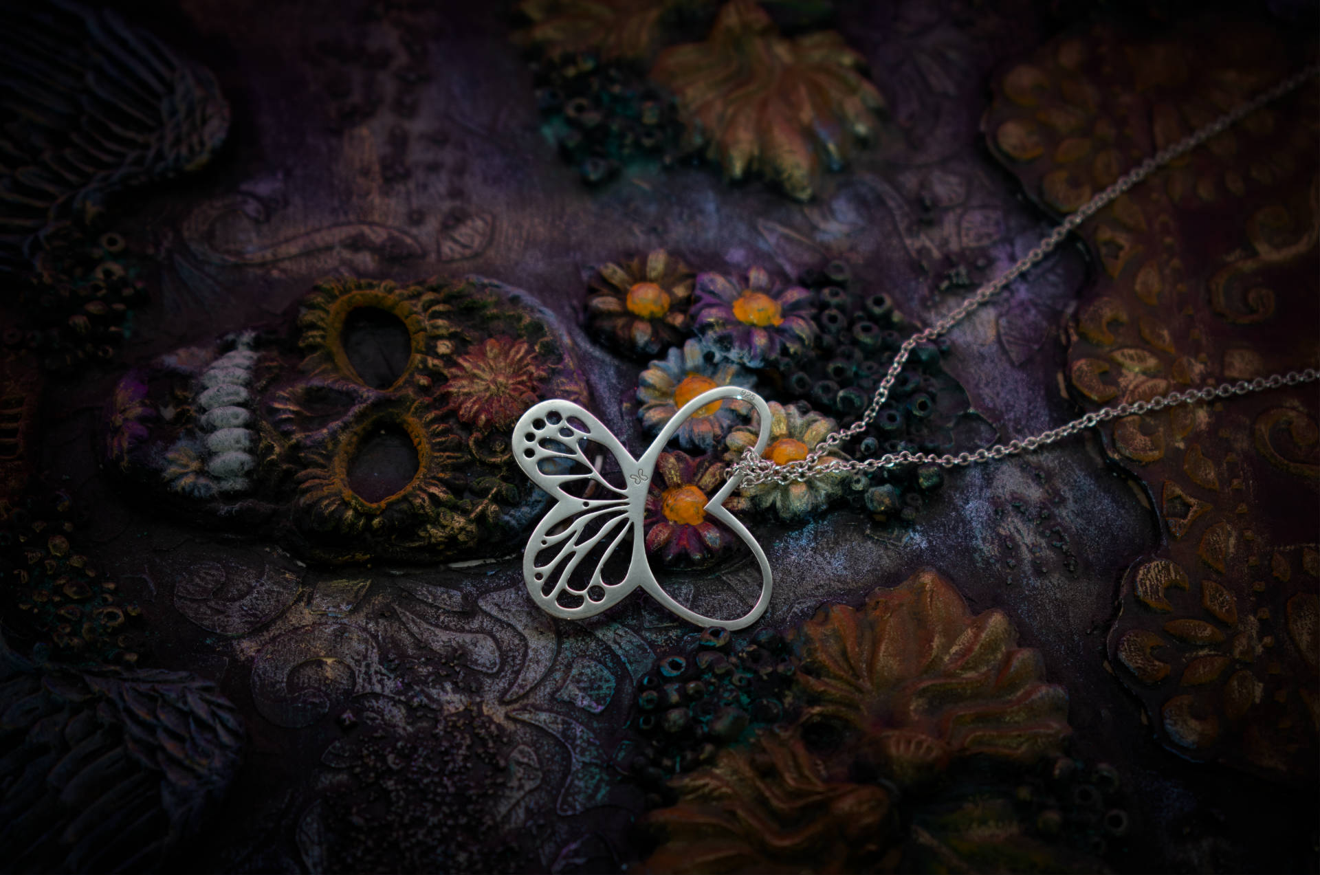 Fotografía primer plano un collar de mariposa Tanya Moss sobr eun fondo temático del Día de Muertos.