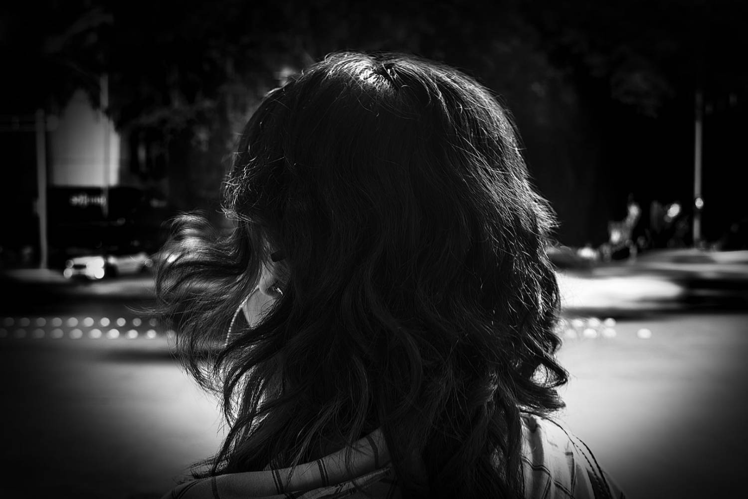 Fotografía primer plano en blanco y negro de una joven de espaldas viendo hacia una avenida.