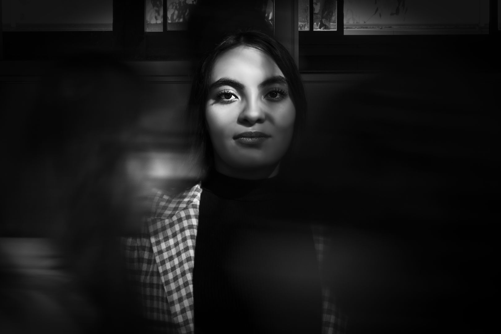 Fotografía plano medio en blanco y negro de una joven con personas barridas pasando frente y detrás de ella.